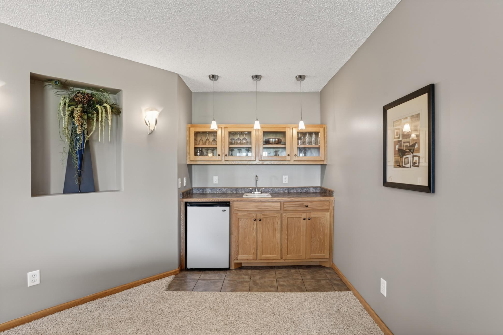 Lower-level wet bar with beverage fridge, upper display cabinetry, and additional serving space