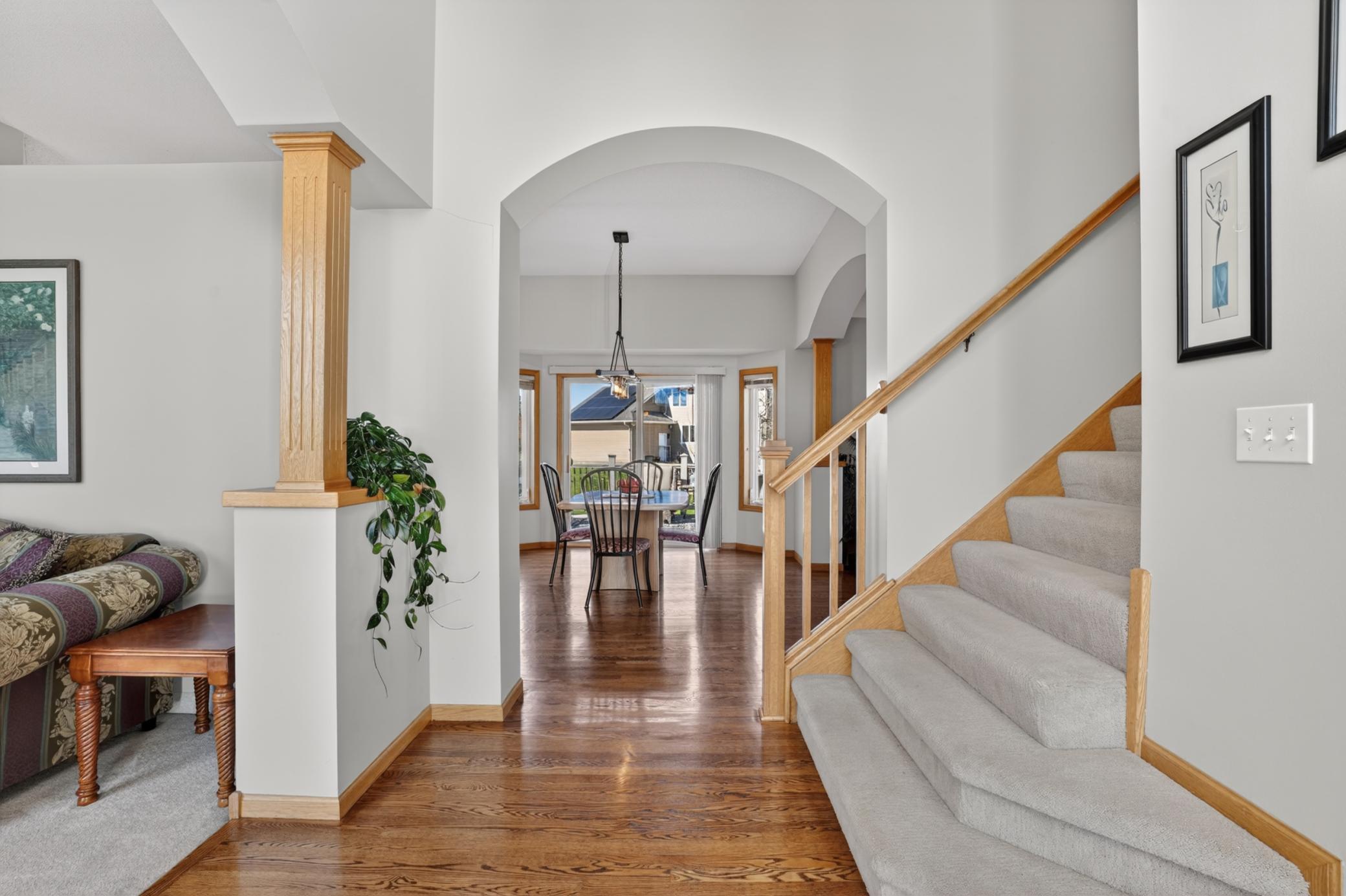 Wide entry with hardwood floors, open staircase, and architectural columns