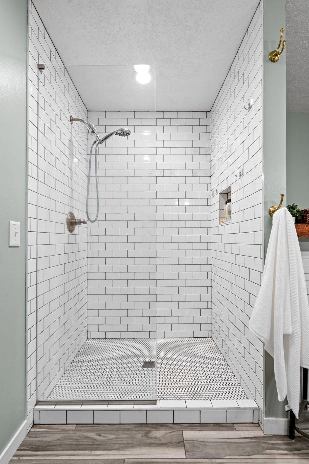Stunning walk-in shower with floor-to-ceiling subway tile, glass surround, and built-in niche storage.