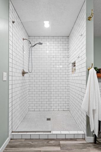 Stunning walk-in shower with floor-to-ceiling subway tile, glass surround, and built-in niche storage.