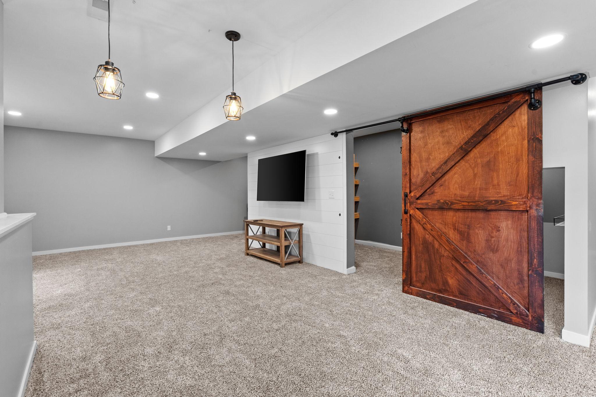 Clean, modern lower level with cozy carpet, recessed lighting, and custom barn door detail