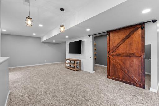 Clean, modern lower level with cozy carpet, recessed lighting, and custom barn door detail