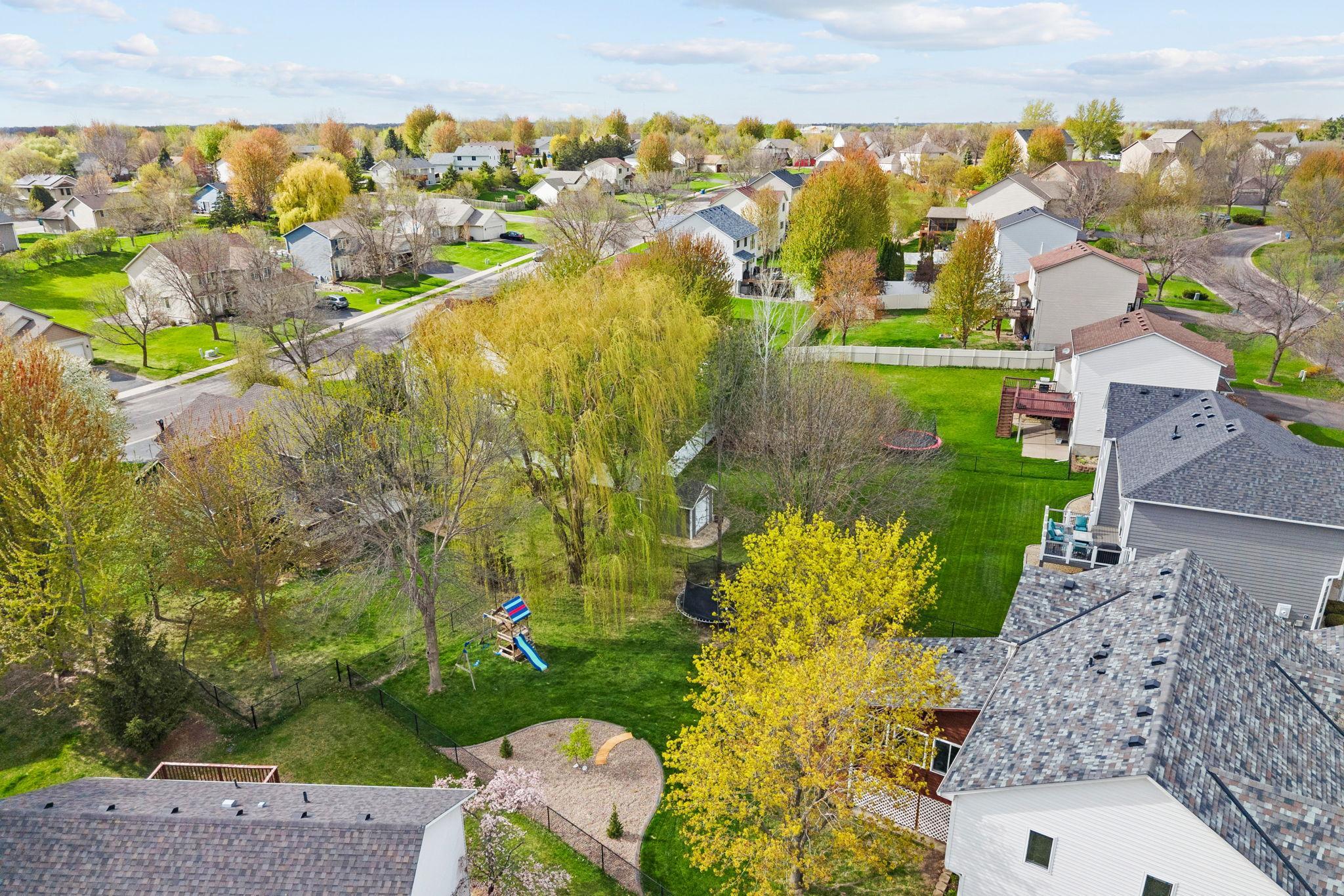 Fully fenced yard with beautiful mature trees, play space, and a patio ready for summer gatherings