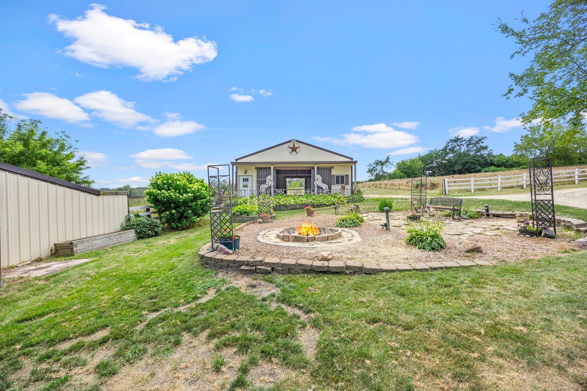 Landscaped fire pit area in front of home near barns.