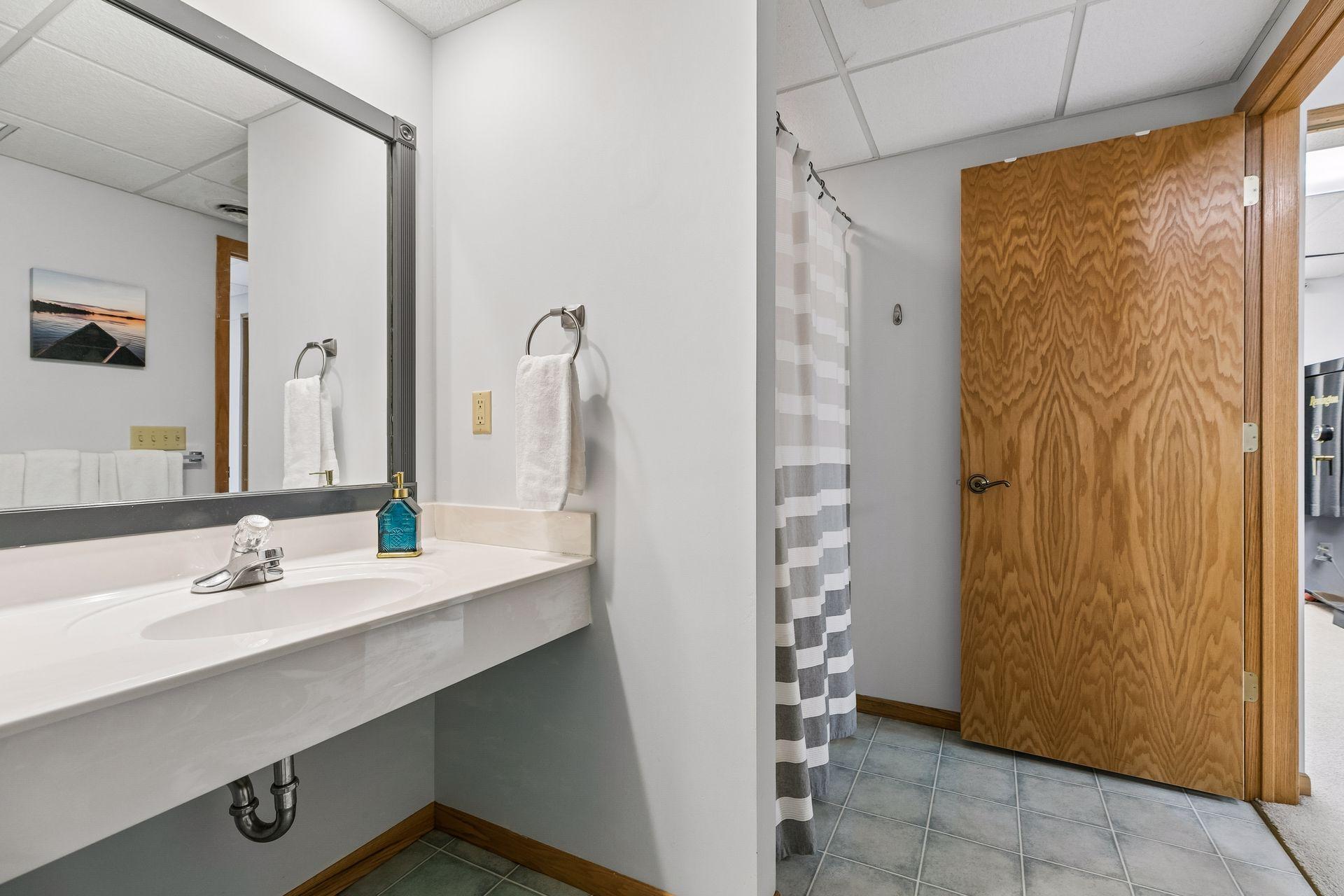 Nice sized lower-level 3/4 bath, with linoleum floors, new toilet, stylish sink and large mirror, offering a functional layout for everyday use and guest convenience just off the family room.