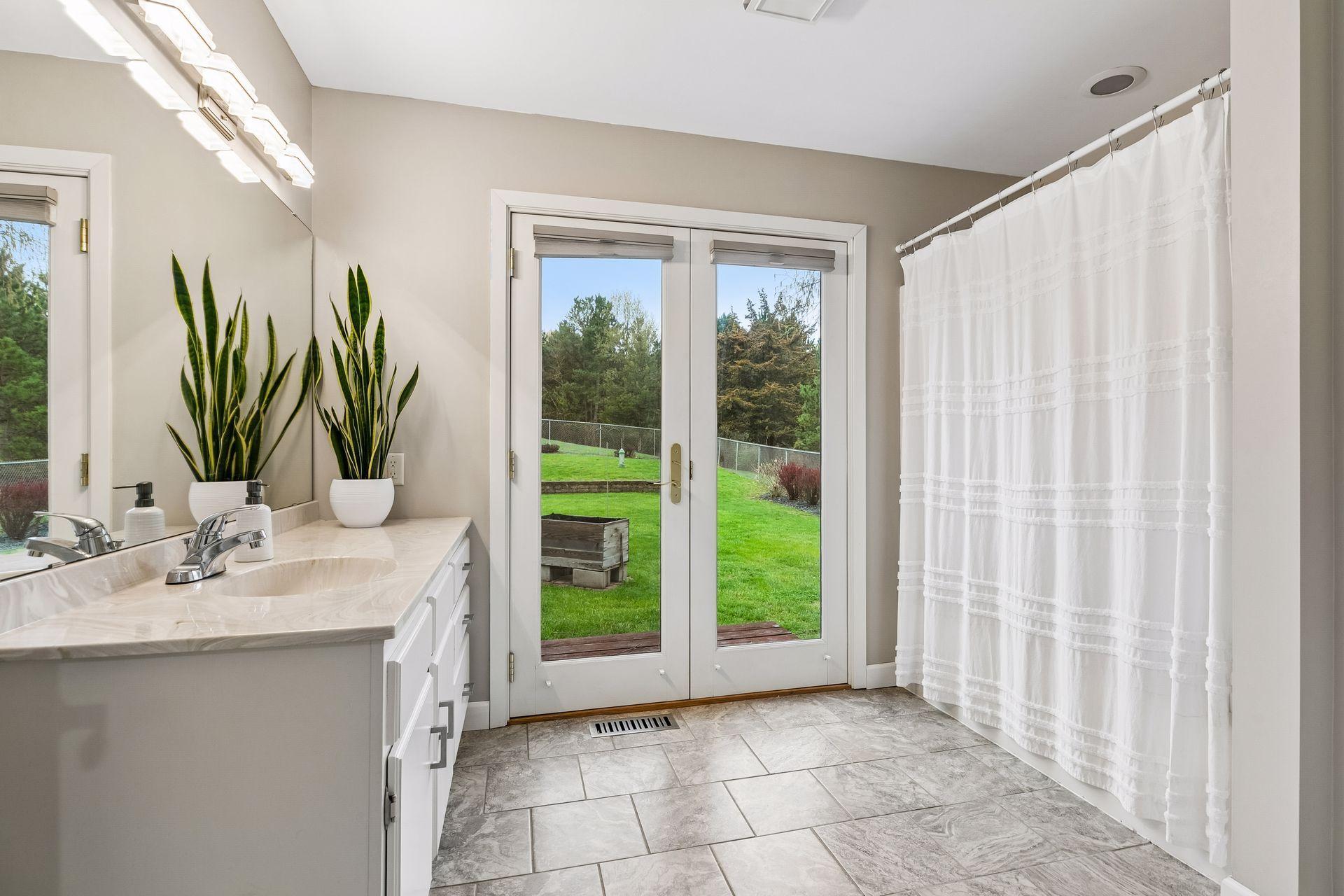Generous main floor bath with a tub/shower combination, vanity sink, wall lights, and French doors opening to the outdoor area.
