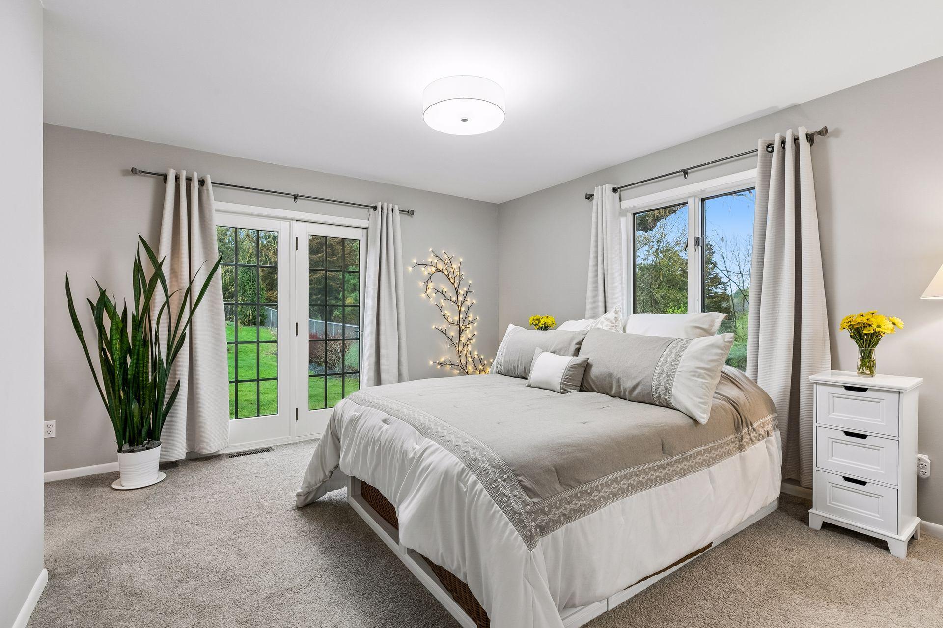 Spacious main level primary bedroom, complete with carpet floors, double doors to the exterior, windows for natural light, overhead lighting, ensuite bathroom, and nice closet.