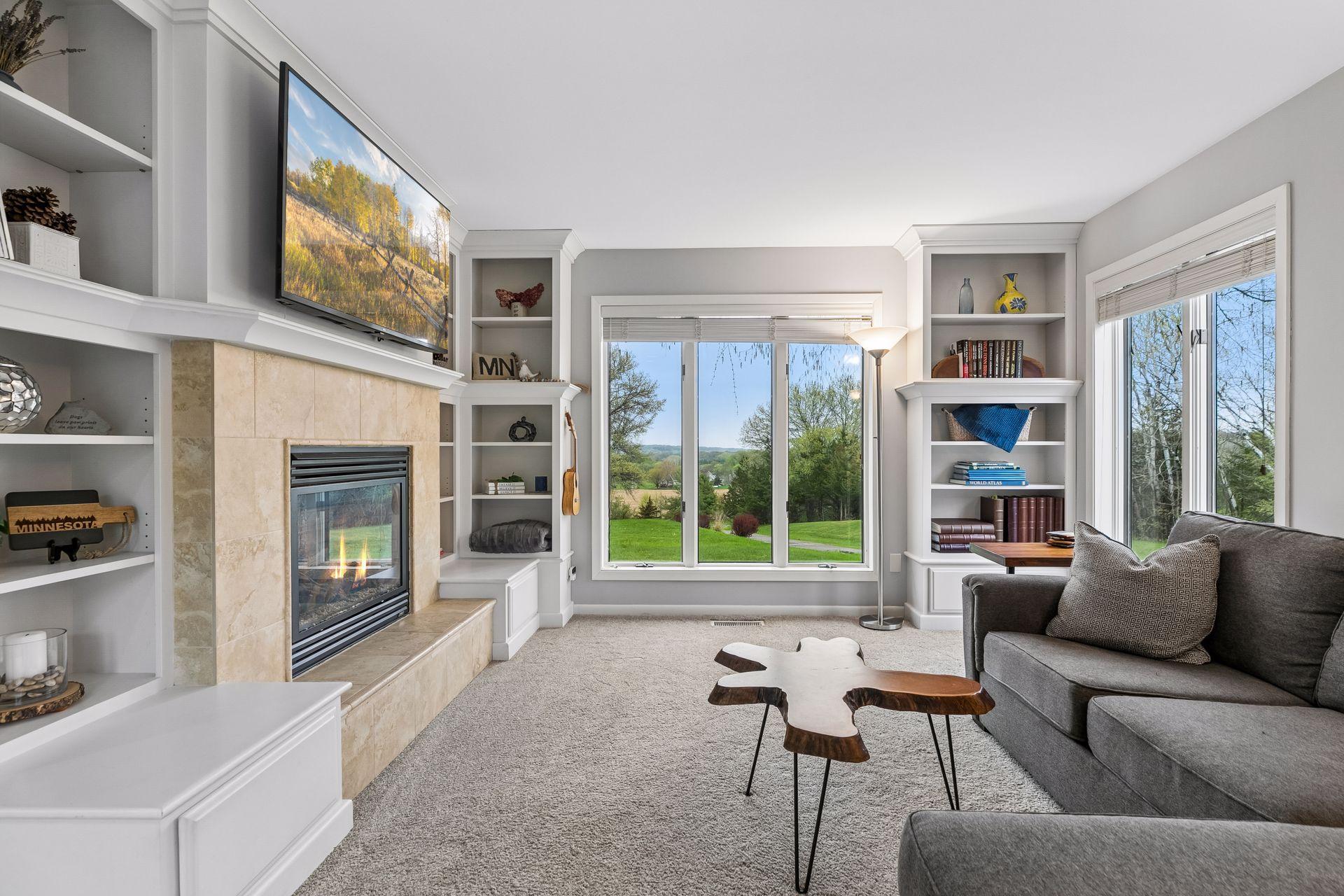 Freshly painted inviting living room featuring stylish built-in bookshelves, cozy carpet flooring, a gas fireplace, and five generous windows filling the space with natural light.