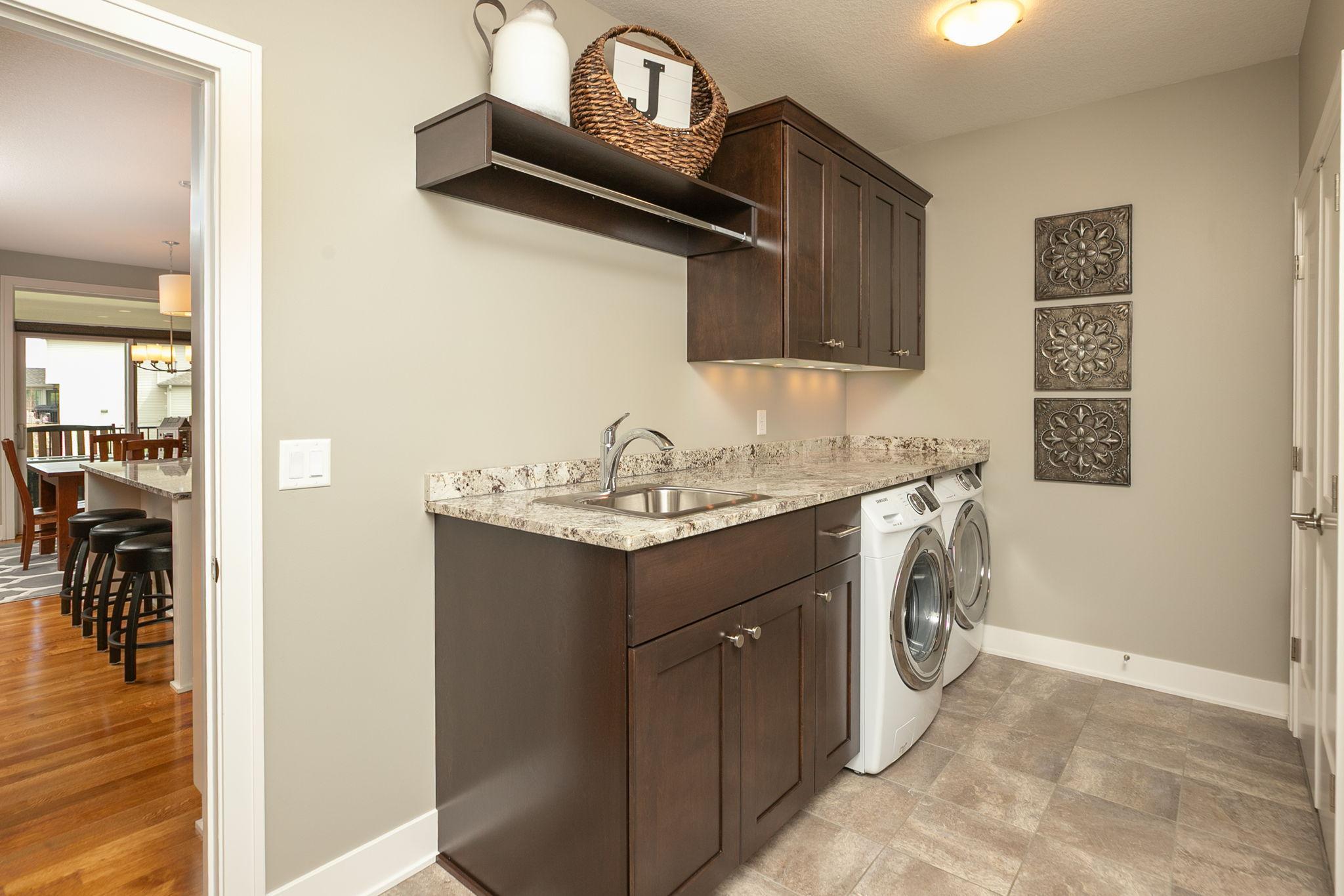 Main floor laundry w/ tub and additional storage cabinets and granite folding table