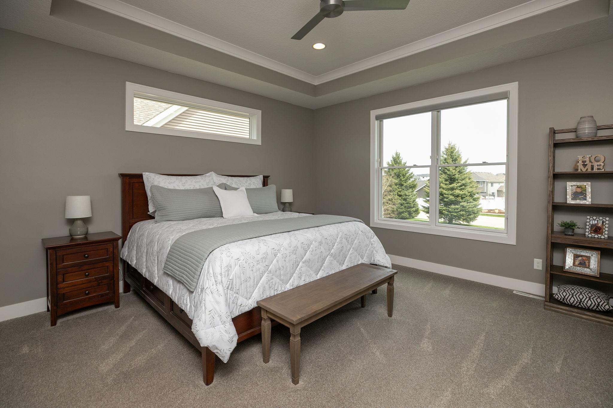Primary bedroom with transom window above the bed and crowned tray ceiling plus a fan