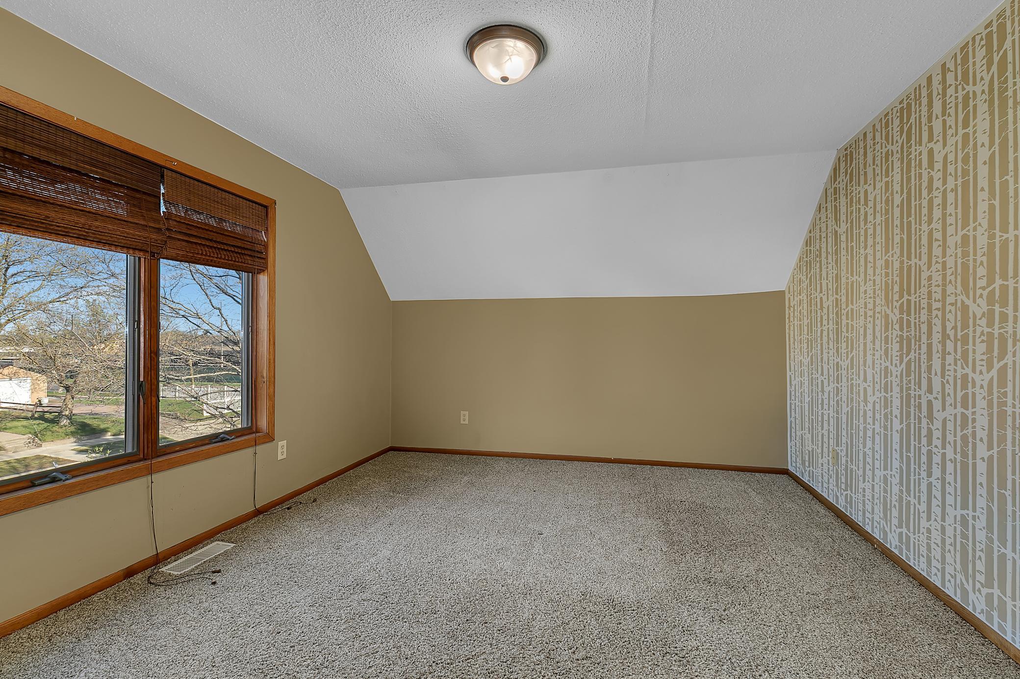 The primary bedroom also features a ceiling light fixture, windows for catching evening breezes and carpet flooring.