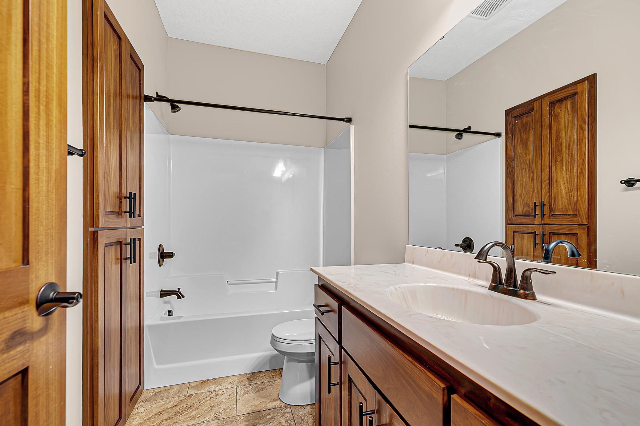 The main level full bathroom has a custom vanity, tiled flooring and a built-in linen cabinet.