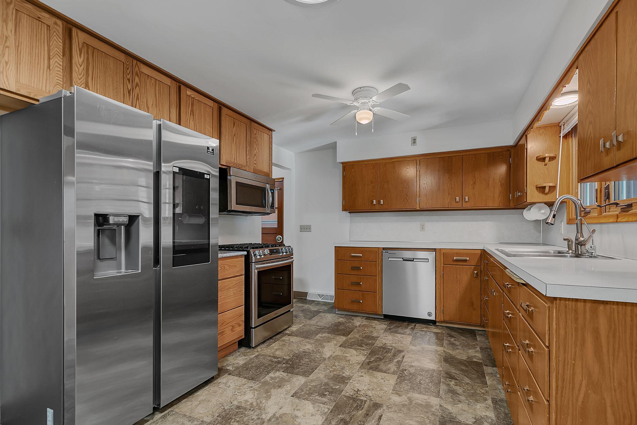 functional kitchen featuring abundant solid wood cabinetry, updated stainless steel appliances including a side-by-side refrigerator, built-in microwave, and gas range, plus a dishwasher for convenience. Spacious L-shaped layout offers ample counter