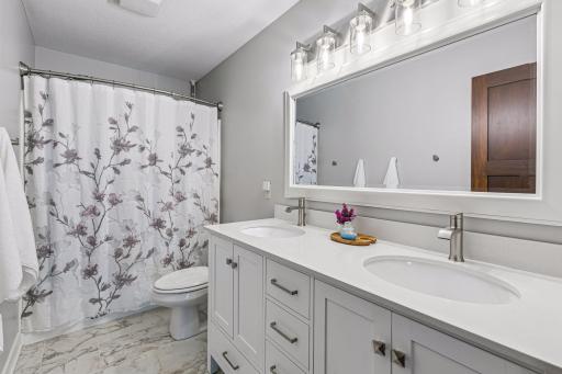 The updated upper-level full bath showcases a stylish double vanity with quartz countertops, modern fixtures, generous storage, and a tub/shower combinationâperfect for family or guests.