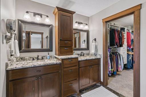 The spa-inspired primary bathroom features heated floors, dual granite-topped vanities with tip-outs, abundant cabinetry with hidden electrical outlets, updated lighting, and direct access to the spacious walk-in closet.