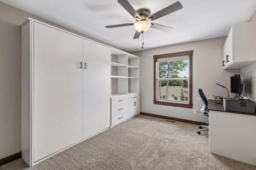 A spacious secondary bedroom offers abundant natural light, plush carpeting, and custom built-in storage with a Murphy bed (can stay or go), allowing the room to easily function as a guest suite, office, or hobby space. TV on wall stays.