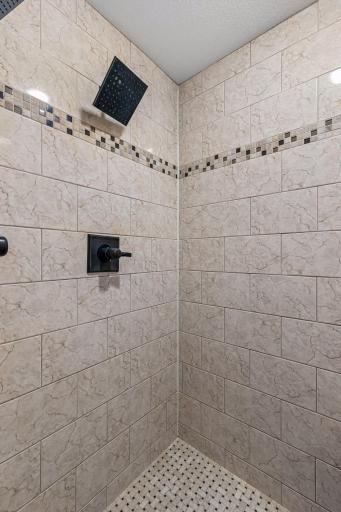 The beautifully tiled walk-in shower showcases elegant ceramic tile surround, decorative accent detailing, and a modern rainfall showerhead for a relaxing spa-like experience.