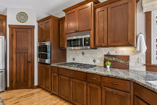 Cooking is a pleasure in this well-equipped kitchen. Features include a five-burner gas cooktop, built-in vented microwave, double oven, walk-in pantry with storage shelving, and tiled backsplash.
