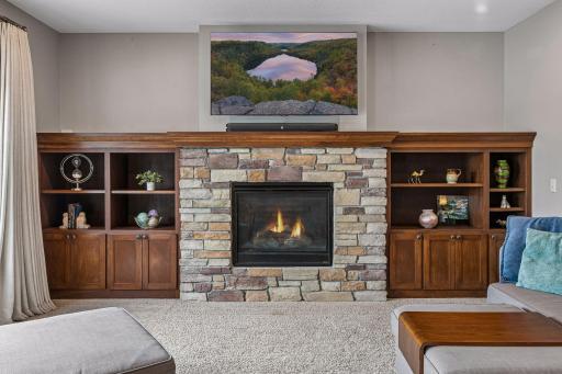 A beautiful stone fireplace serves as the focal point of the family room, flanked by custom built-in cabinetry and display shelving that provide both character and functional storage.