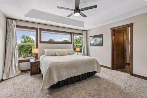 Escape to the spacious primary suite, featuring a tray ceiling, plush carpeting, a ceiling fan, abundant natural light, and oversized windows that create a bright, peaceful retreat.