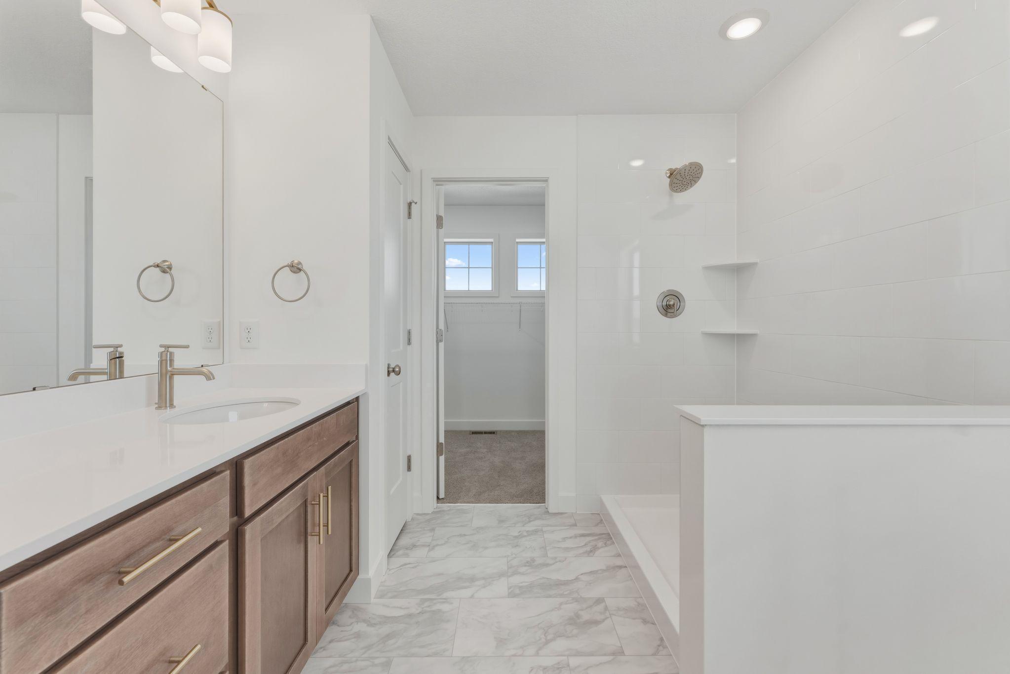 Owner's bathroom with double vanity, tiled shower, and linen closet leading to walk-in closet