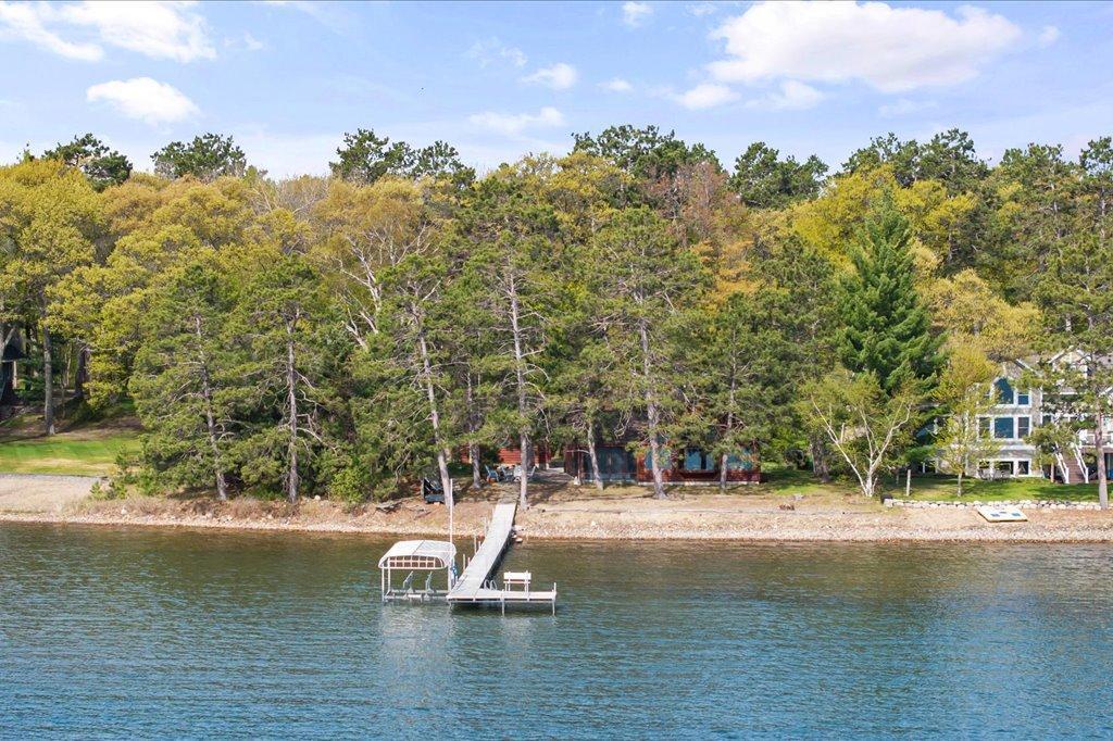 Aerial view highlighting the private wooded setting, sandy shoreline, and dock extending into the lake.
