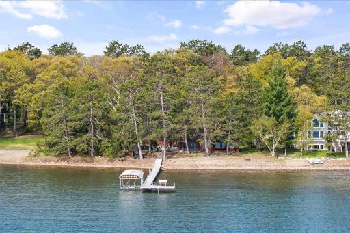 Aerial view highlighting the private wooded setting, sandy shoreline, and dock extending into the lake.