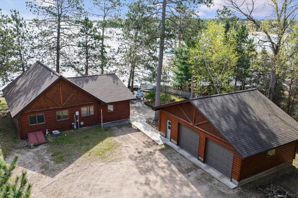 Aerial view showcasing the cabin, detached garage, and lakeside setting among mature trees.