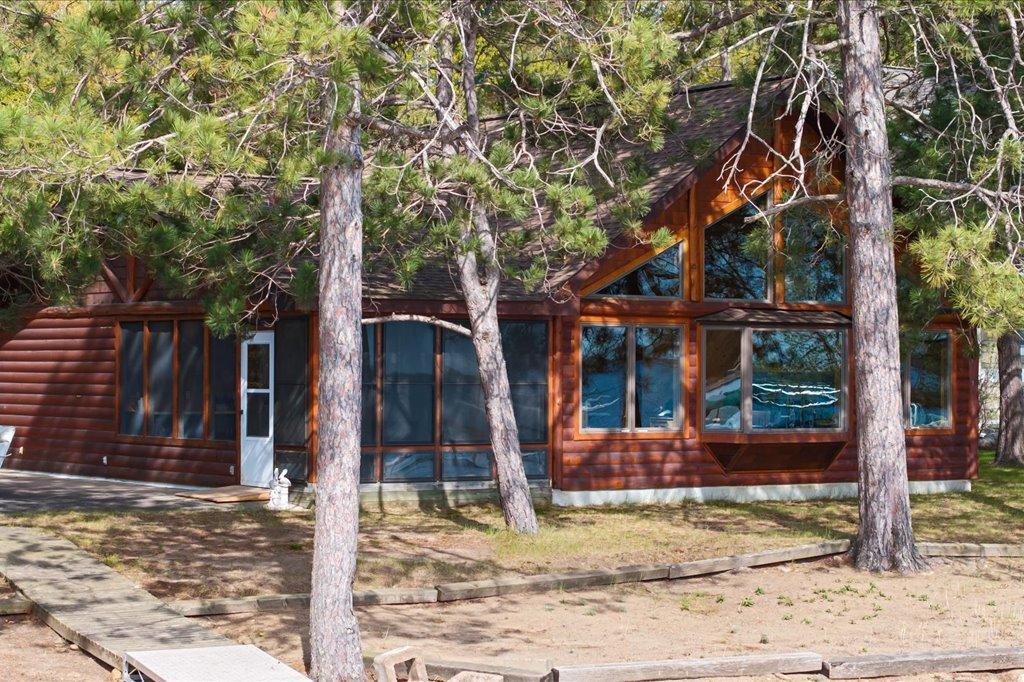 Classic log-sided cabin nestled among mature pines with expansive lakeside windows.