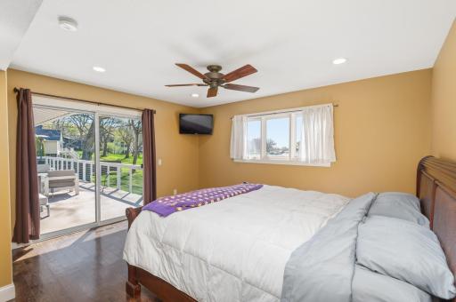 The main floor primary bedroom faces the lake and steps out to the large deck. Notice wood plank floors, recessed lighting and ceiling fan.