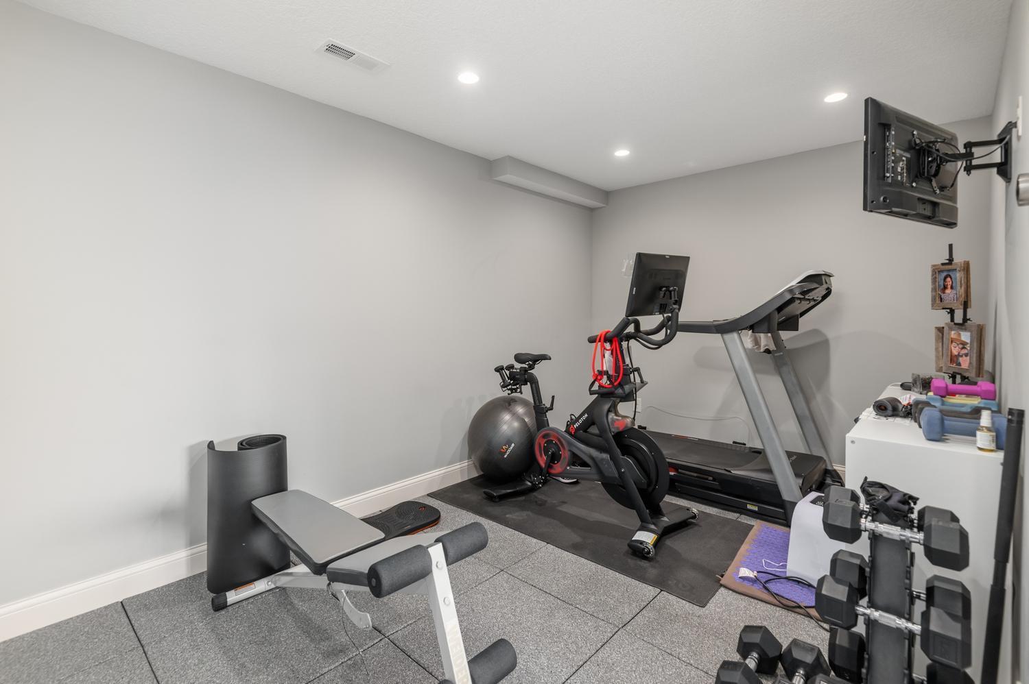 Bright exercise room with recessed lighting, TV and padded floor.