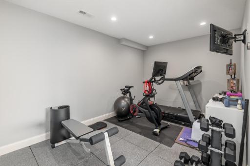 Bright exercise room with recessed lighting, TV and padded floor.