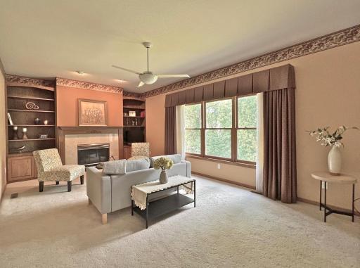 nviting family room featuring a fireplace, built-in cabinetry, neutral carpeting, and large windows