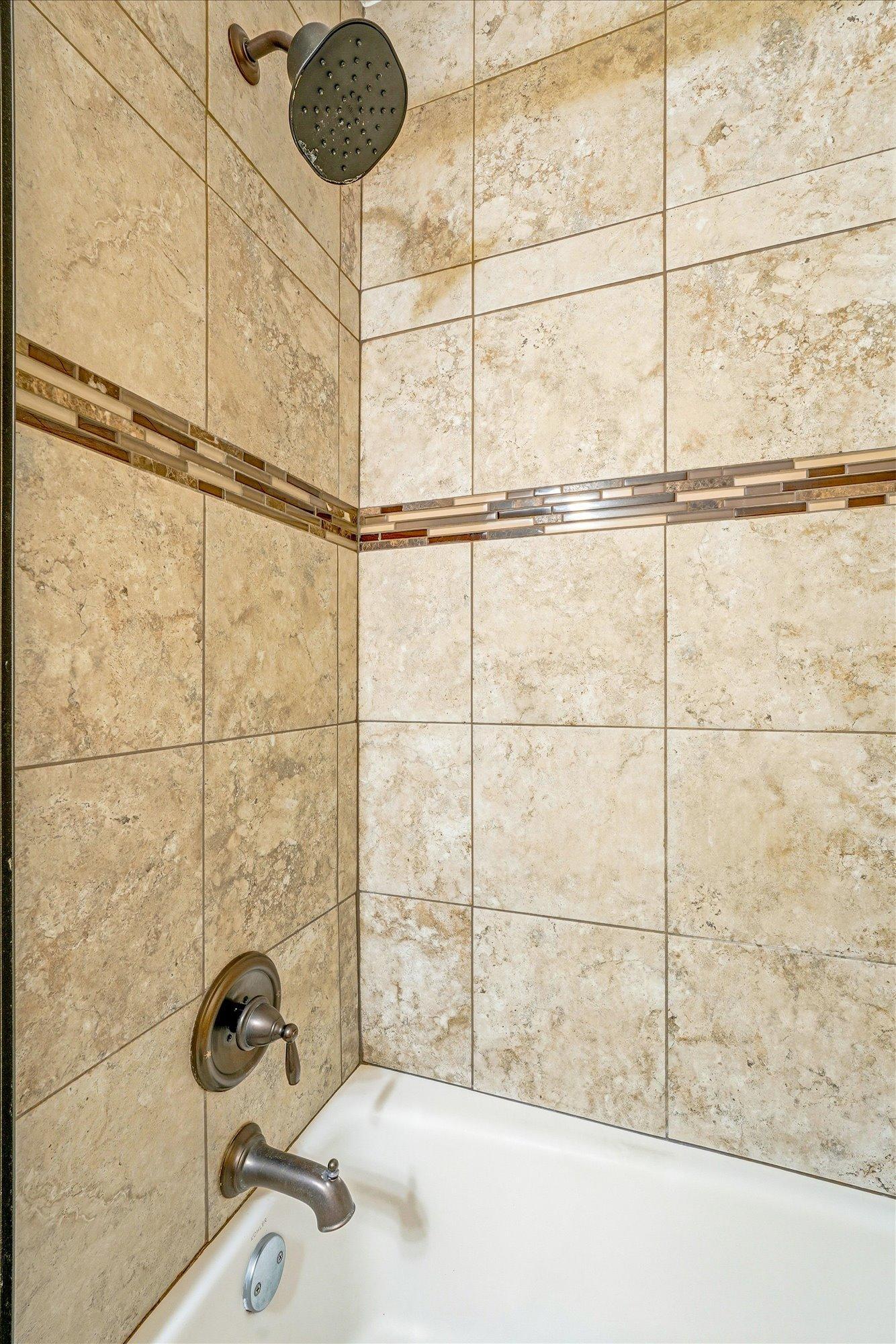The updated bathroom features elegant tilework and a sleek glass shower door.