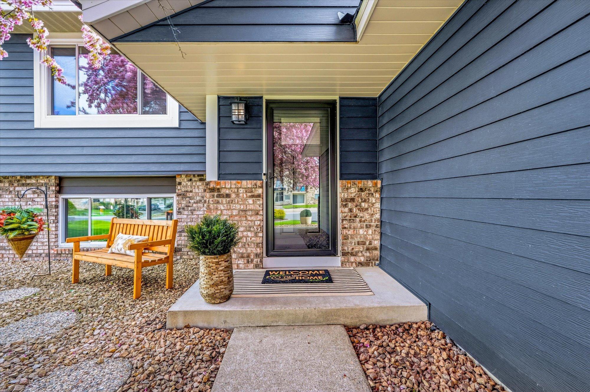 Inviting front entrance featuring a storm door, maintenance-free landscaping, and charming sitting area.