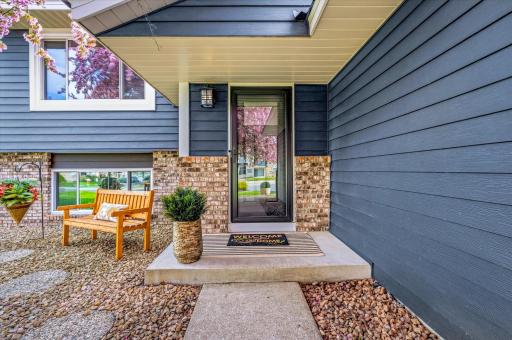 Inviting front entrance featuring a storm door, maintenance-free landscaping, and charming sitting area.