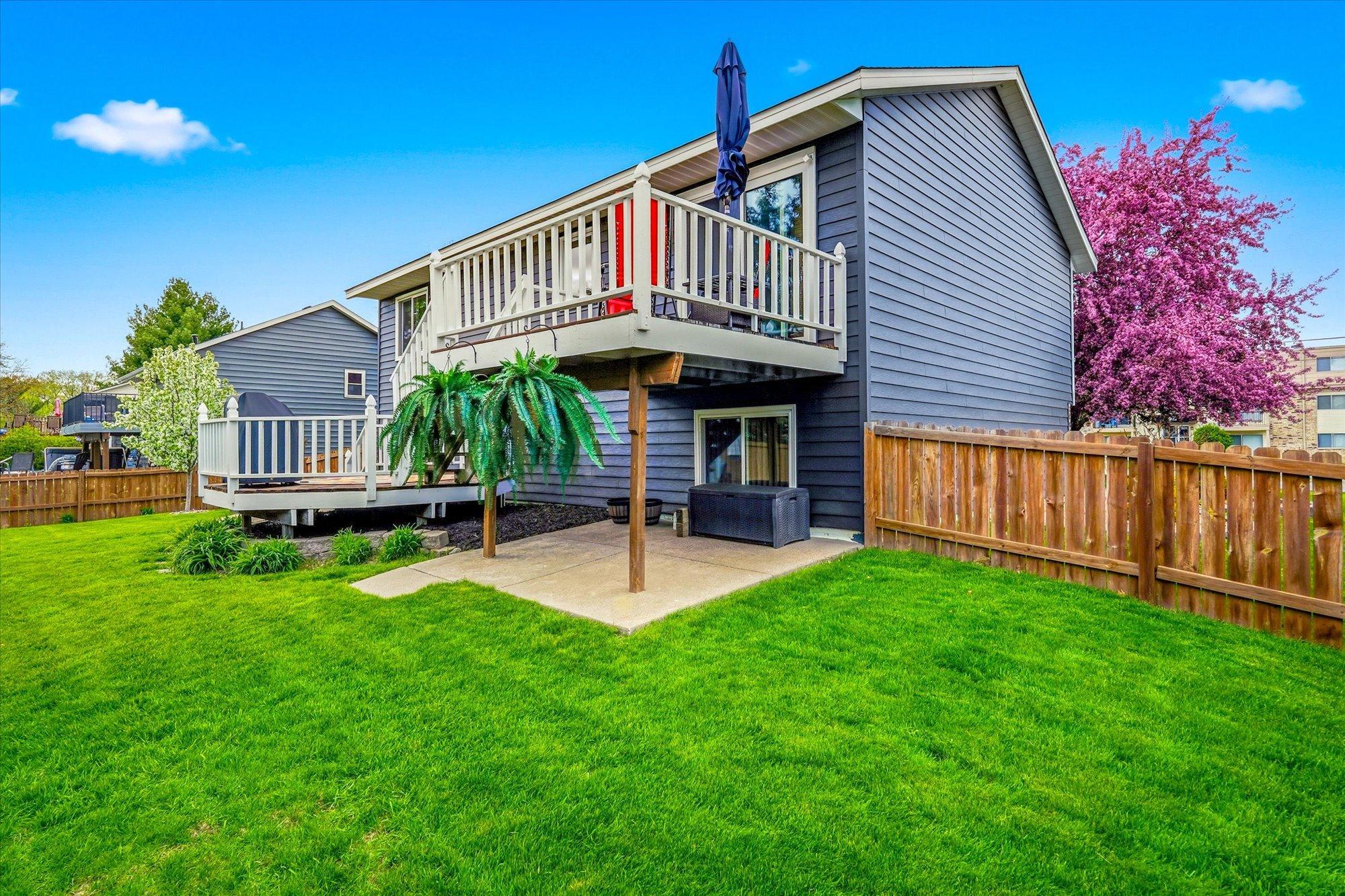 Another view of the backyard showcasing the oversized deck, lower patio, and fenced yard.