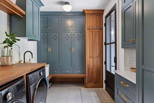 Upscale laundry and mud room provides lockers, storage cabinets, farmhouse sink, drying rack, and a bench. The door leads to the garage.