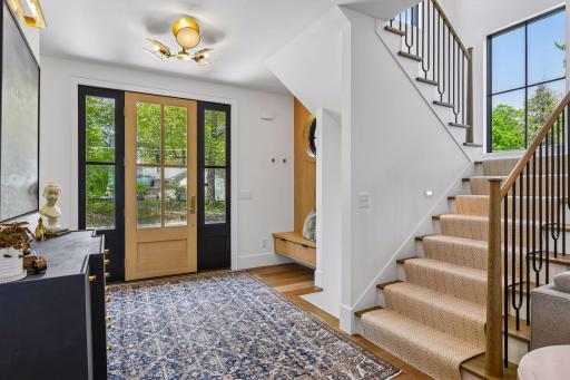 Expansive foyer with storage bench and a cute window offering a nautical touch to the lake home. Patterned wool carpet runner on the stairs.
