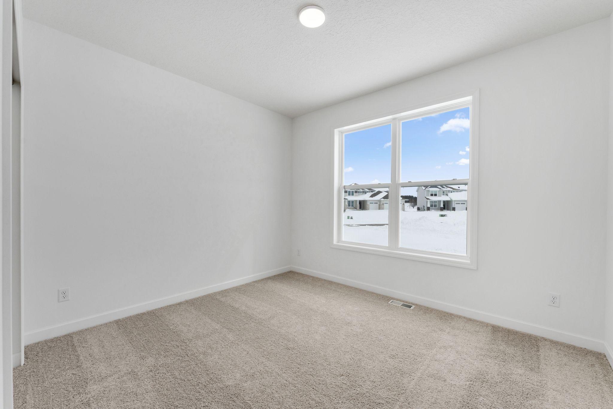 (Photo of a similar home, actual finishes may vary) Overlooking the front of the home, this secondary bedroom enjoys natural light streaming in through its tall windows. It includes plush carpeting and a wardrobe closet.