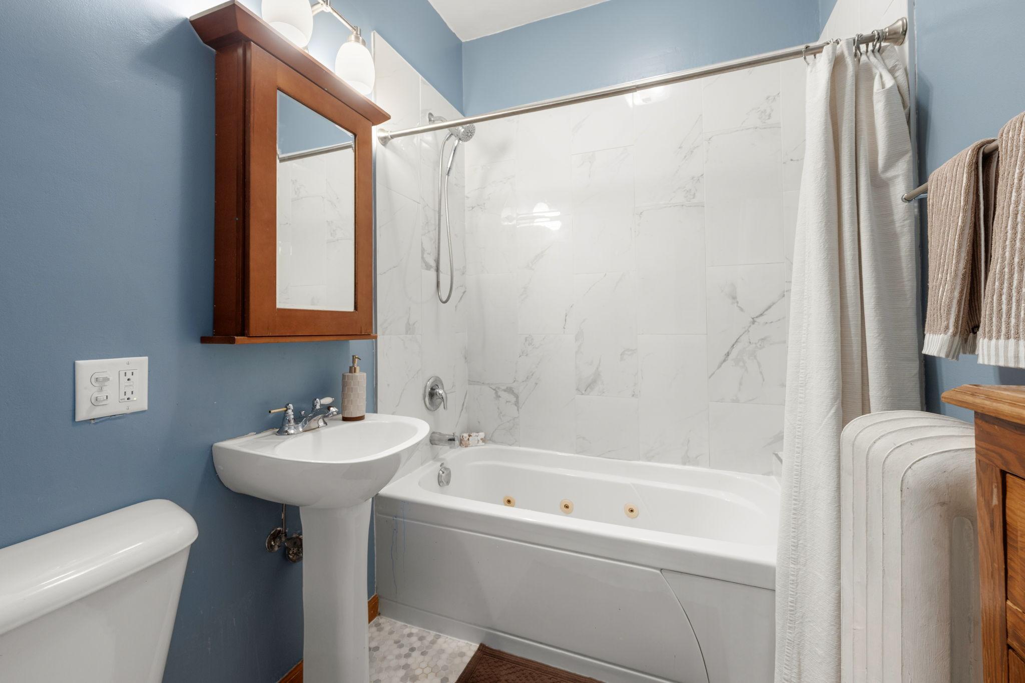 Main level full bathroom with jetted tub and tile surround.