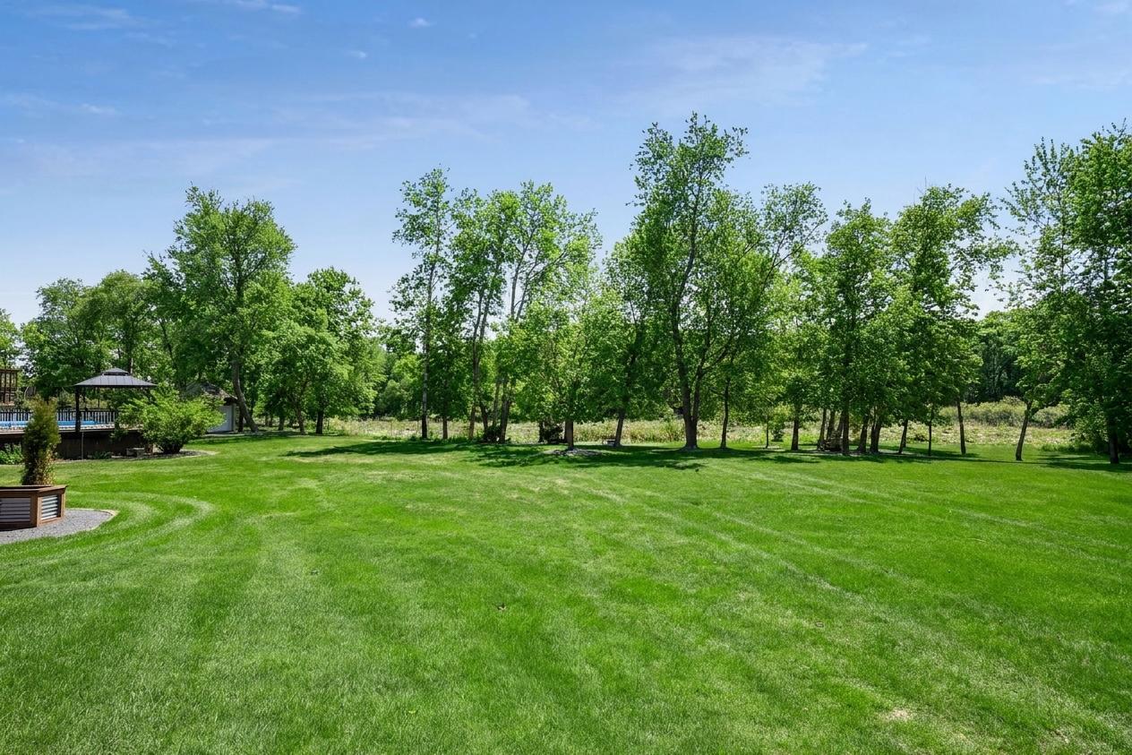 Expansive backyard with lush green lawn, mature trees, and peaceful nature views creating a private park-like setting.