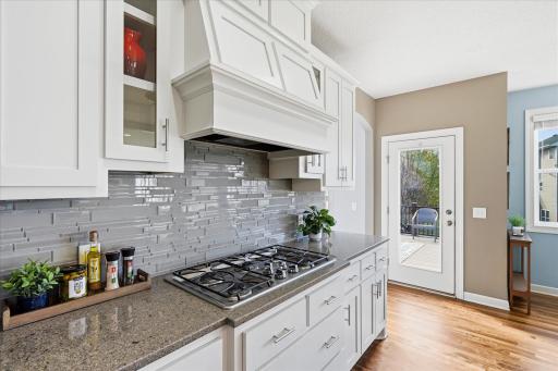 A custom range hood anchors the cooking area and is framed by glass backsplash.