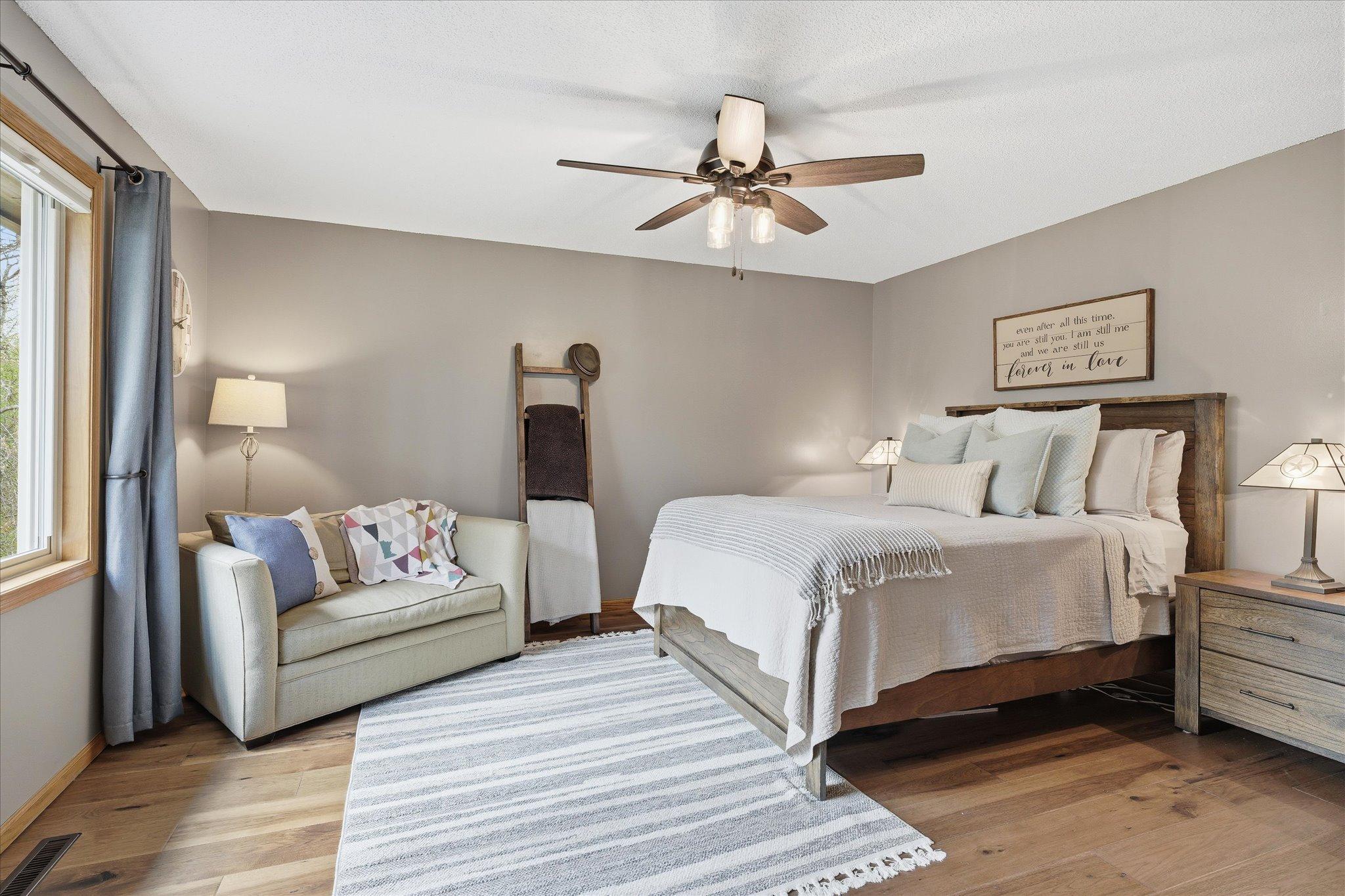The primary bedroom has engineered hickory hardwood floors, neutral paint, a modern ceiling fan and top-end window treatments.