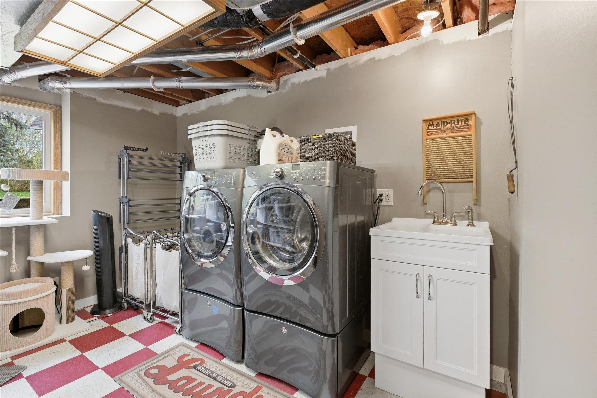 The finished laundry room has a sink, high end Electrolux laundry machines, extra lighting from above and from the window.