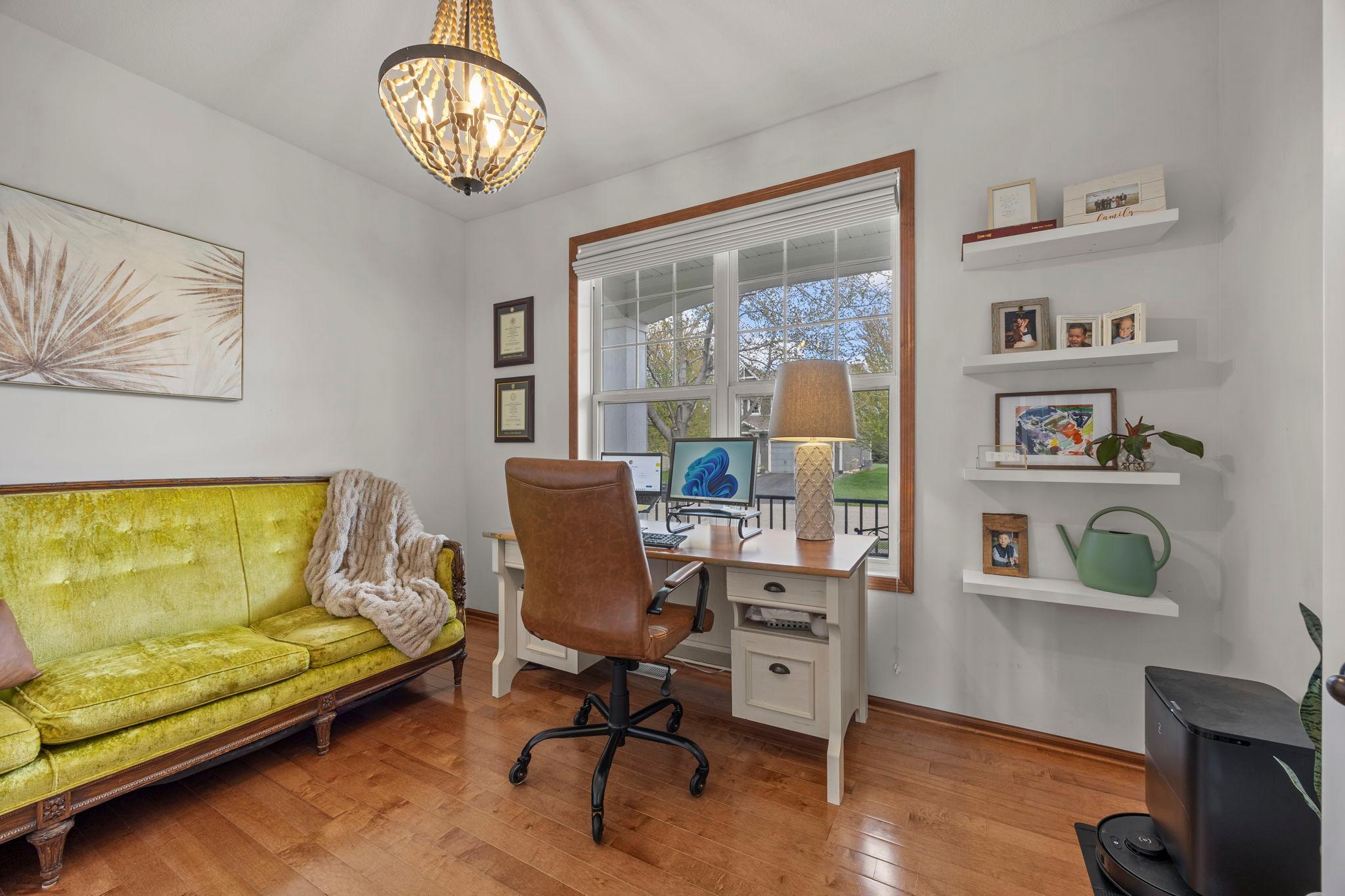 To the right, a spacious office or den is enclosed by French glass doors and highlighted by a unique hanging light fixture and a large front-facing window.