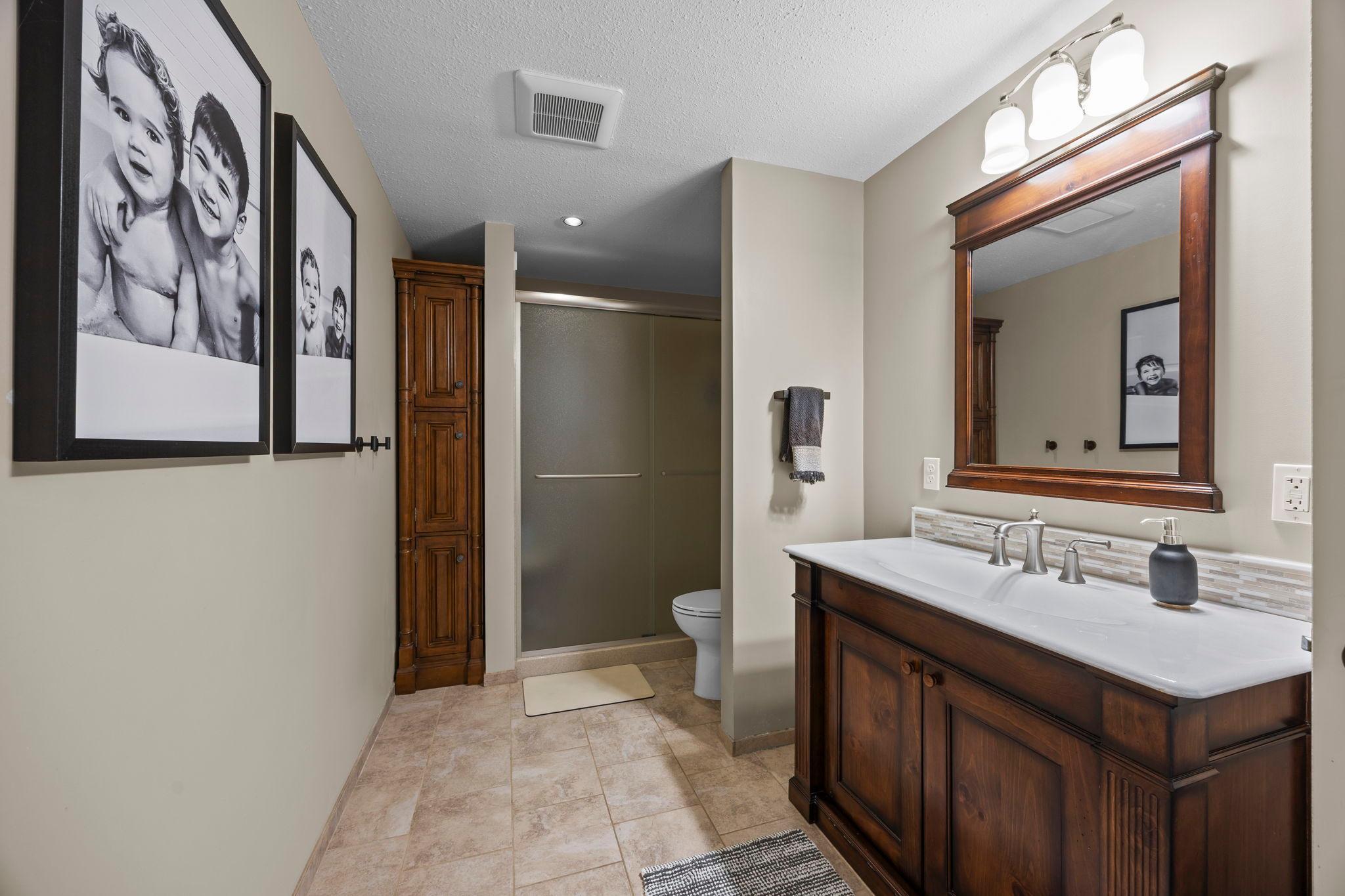 Nearby a three-quarter bathroom that includes tile flooring, a walk-in shower, and a single vanity.