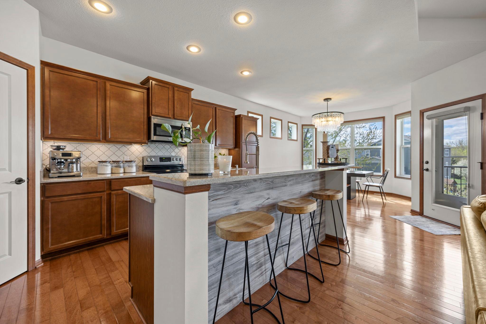Further down the hall, the kitchen boasts ample wood cabinetry, granite countertops, a breakfast bar, stainless steel appliances, and a walk-in pantry.