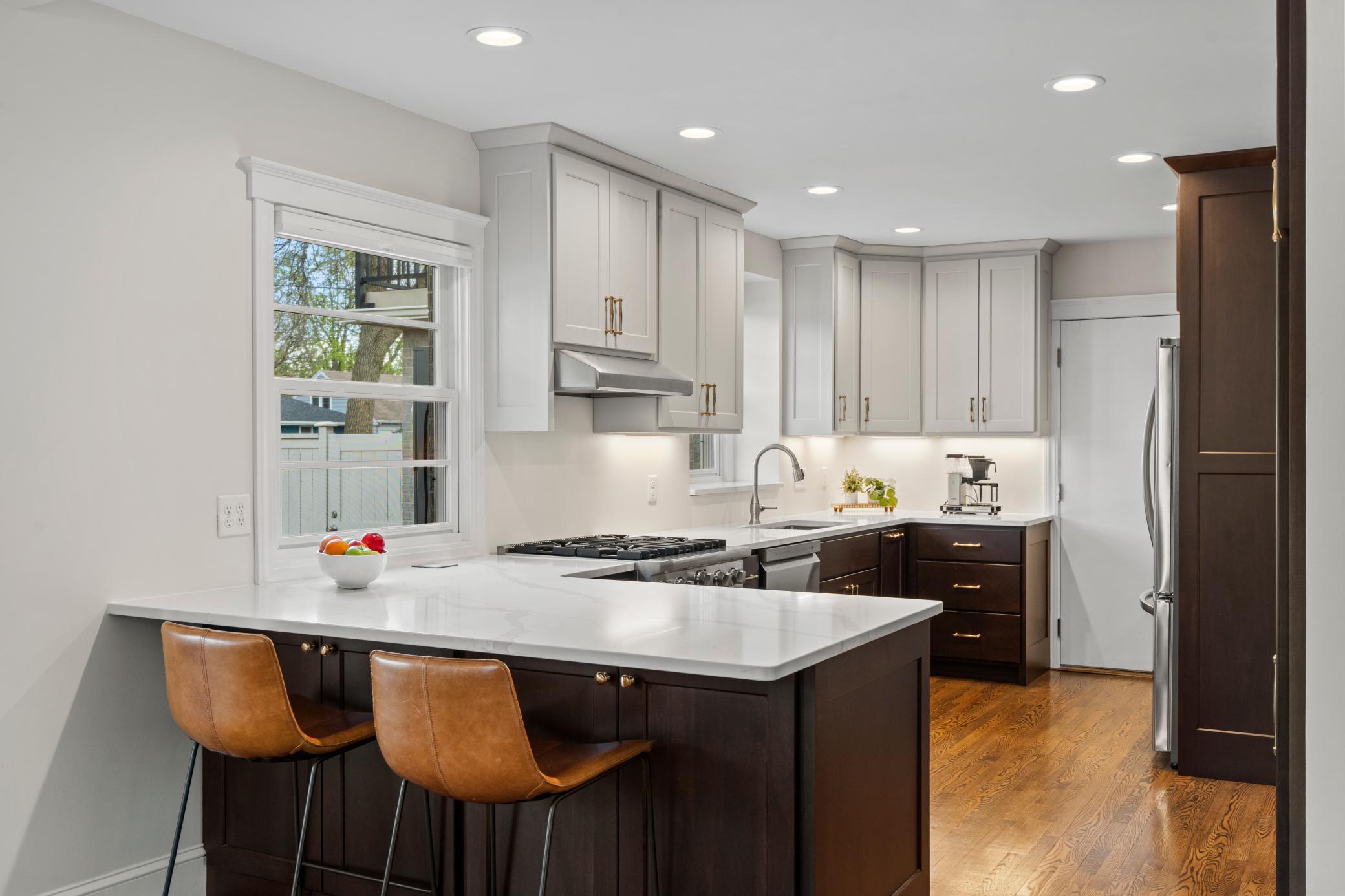 The beautifully updated kitchen features custom soft-close cabinetry with rollouts, quartz countertops with breakfast bar seating, and stainless-steel appliances—including a Viking gas range with hood, newer refrigerator, and dishwasher.