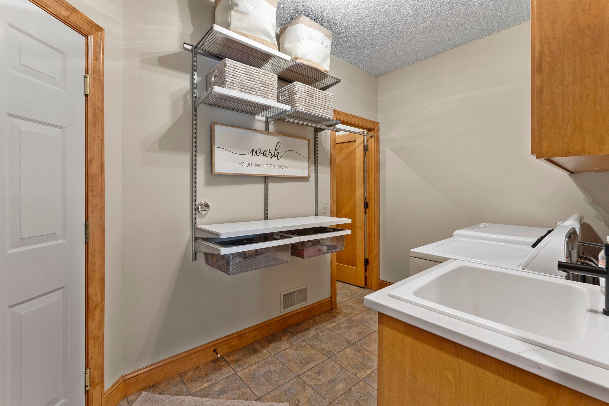 The main-level laundry room complete with ample cabinetry, shelving for organization, a sink, a large walk-in closet, and access to the attached three-car garage.